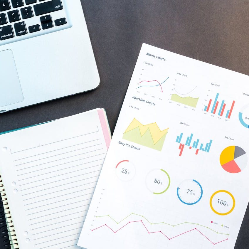 Flatlay of business report with colorful charts, a notebook, and a laptop for data analysis on a desk.